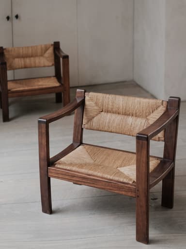 An armchair constructed with a dark-stained solid wood frame and natural woven rush for both the seat and backrest. The frame features a robust, rectilinear design with wide, flat armrests, and the woven material provides a textured surface. — 3D model