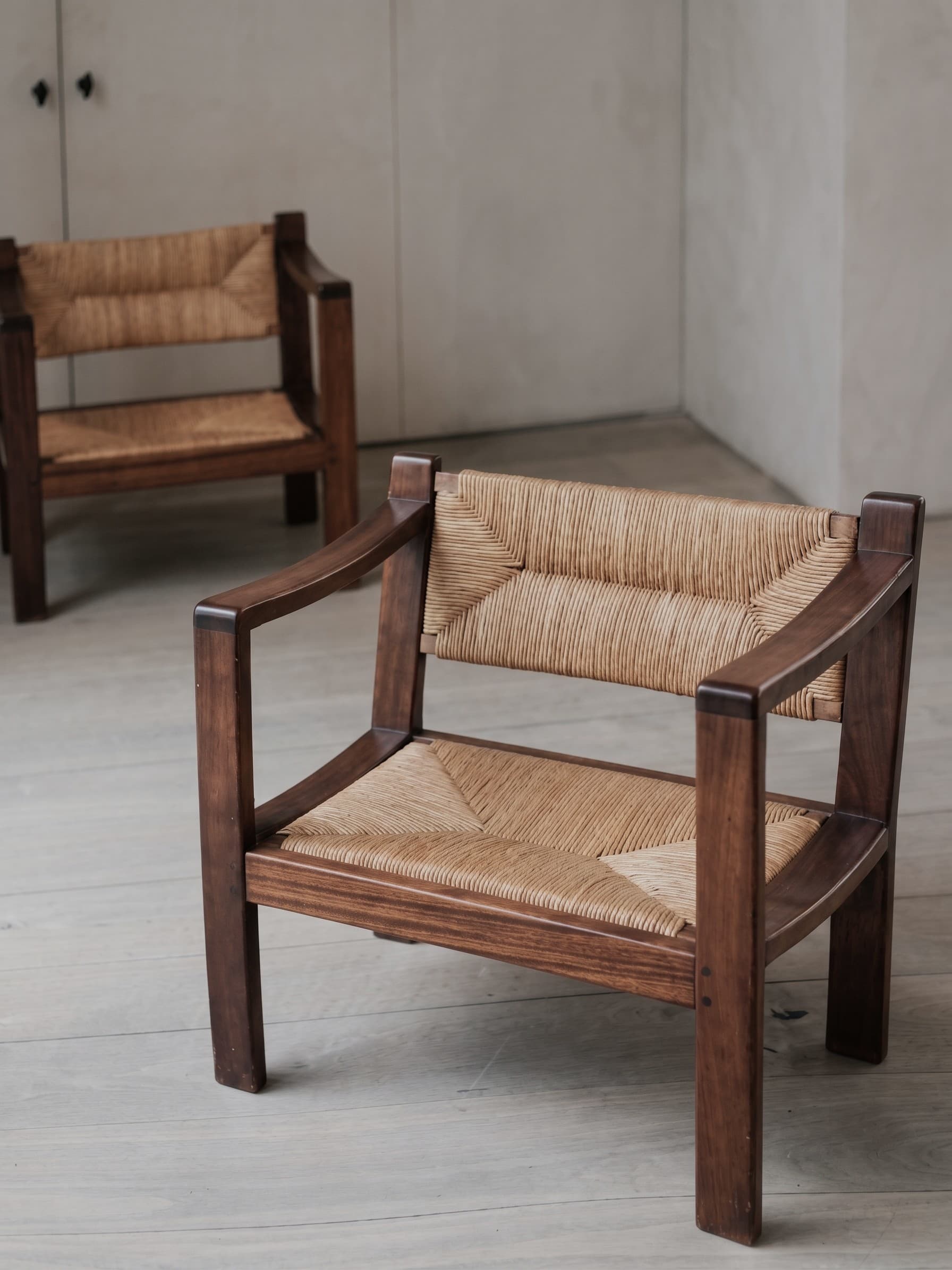 An armchair constructed with a dark-stained solid wood frame and natural woven rush for both the seat and backrest. The frame features a robust, rectilinear design with wide, flat armrests, and the woven material provides a textured surface. — 3D model