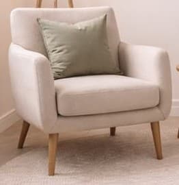 An inviting contemporary upholstered armchair featuring a light beige fabric and a gentle, rounded silhouette. It includes a loose, square sage green accent pillow and stands on four slender, angled wooden legs. — 3D model