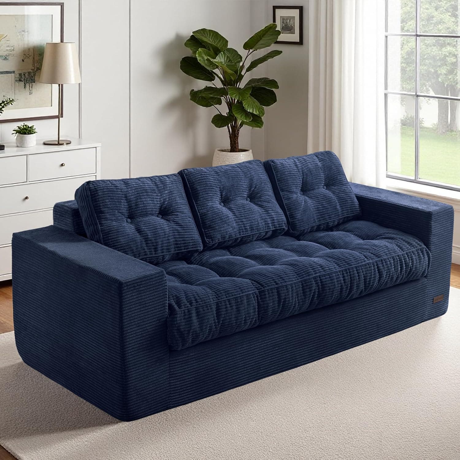A contemporary three-seater sofa upholstered in a navy blue wide-wale corduroy fabric, featuring deep button tufting on the seat and back cushions. The sofa has a substantial, rectilinear frame with wide, flat arms and a low back. The seat cushions are thick and plush, extending slightly beyond the frame. The overall design emphasizes comfort and a modern, relaxed aesthetic. — 3D model