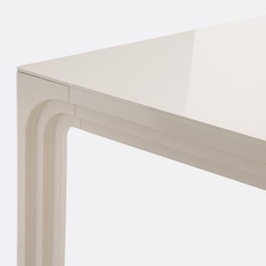 A close-up view of a table's surface and leg. The surface appears to be a high-gloss, off-white material, reflecting light. The leg has a distinctive carved design with layered, curved elements, reminiscent of a waterfall or architectural molding. The overall construction suggests a modern or contemporary style. — 3D model