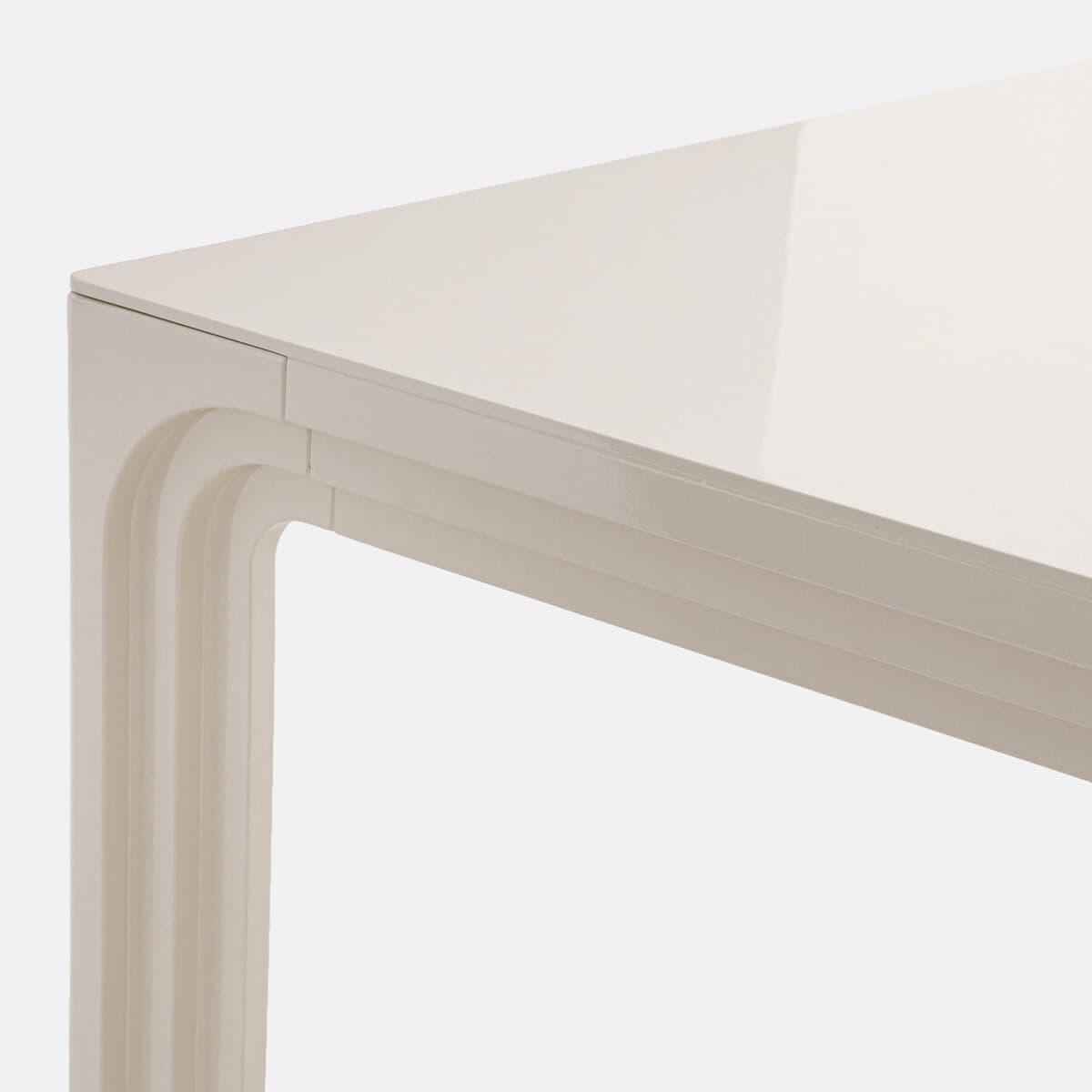 A close-up view of a table's surface and leg. The surface appears to be a high-gloss, off-white material, reflecting light. The leg has a distinctive carved design with layered, curved elements, reminiscent of a waterfall or architectural molding. The overall construction suggests a modern or contemporary style. — 3D model
