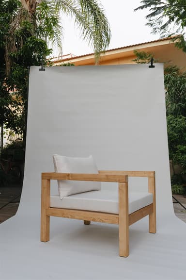 A single armchair with a solid wood frame and upholstered cushions. The frame consists of thick, square-profile wooden beams for the legs, base, and arms. The seat and back are padded with white cushions. A rectangular lumbar pillow is placed against the back cushion. — 3D model