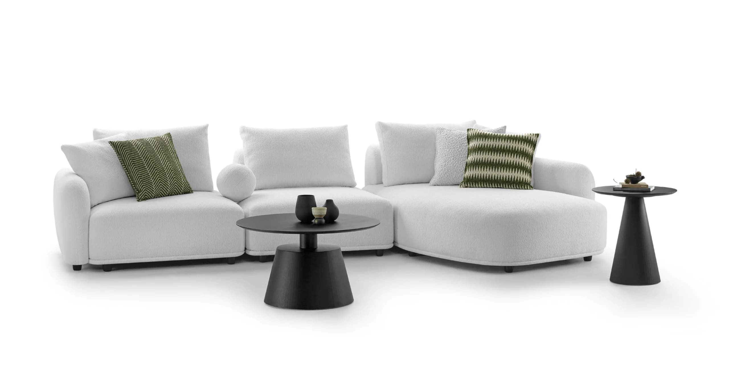 An L-shaped sectional sofa in a white, textured fabric, consisting of multiple modular components, including a chaise lounge end. The sofa features plush, rounded cushions and backrests, accompanied by several matching white throw pillows and three green patterned accent pillows. The design is low-profile and contemporary. — 3D model