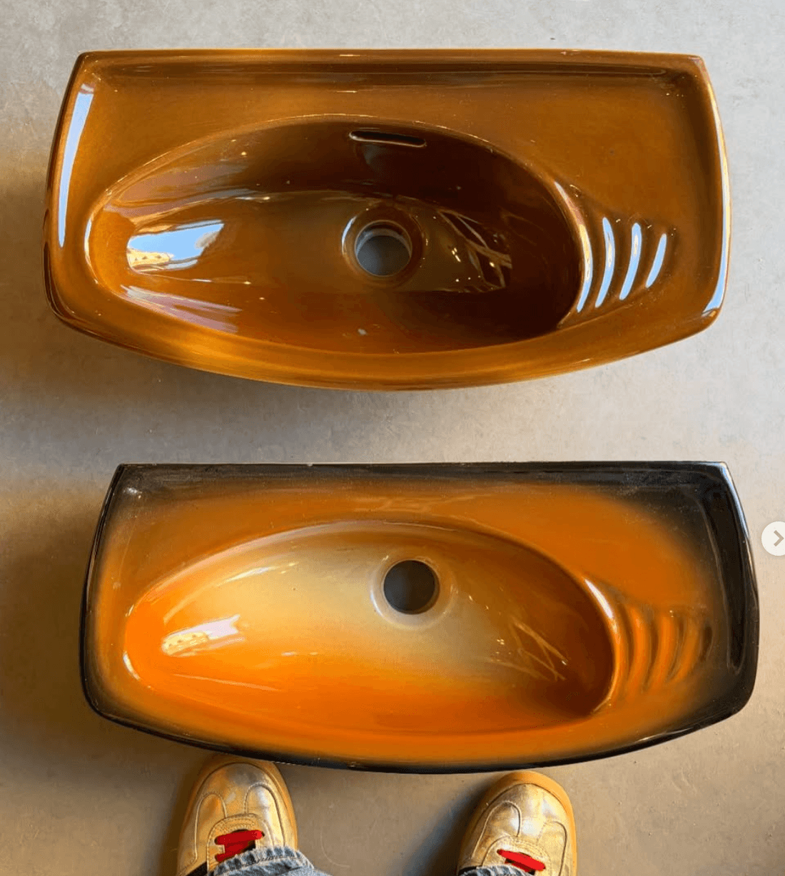 A rectangular bathroom sink featuring a distinctive two-tone ombre finish, transitioning from a dark brown or black at the outer rim to a vibrant orange in the mid-basin, and fading to a lighter beige or cream color at the bottom. The basin has smoothly rounded corners and an integrated overflow slot near the top rim, opposite the drain opening at the center bottom. The surface is highly reflective, indicating a glossy, glazed finish. — 3D model