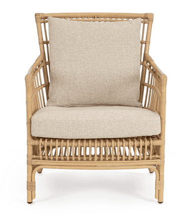 A light brown natural rattan lounge armchair featuring a curved, open-weave frame. It is fitted with thick, removable, light beige upholstered seat and back cushions. The chair has a rounded back and arms, with vertical rattan slats forming the back and side panels. The legs are integrated into the curved frame, with the rear legs slightly flared. The overall aesthetic is natural and relaxed. — 3D model