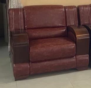 A plush, upholstered armchair in a deep reddish-brown (burgundy) faux leather material, featuring distinctive dark wood armrests with a rounded top and vertically grooved side panels. The backrest shows vertical stitching detail. — 3D model