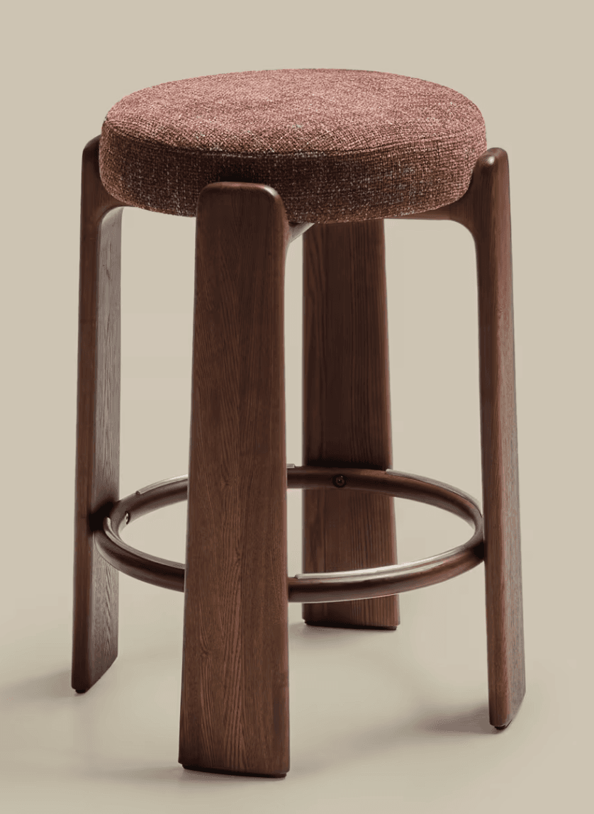 A modern bar stool featuring a round upholstered seat and a dark wood frame with four sculpted legs. An integrated circular metal footrest is positioned for comfort. — 3D model