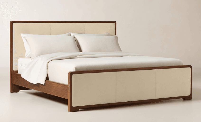 A contemporary bed frame featuring a robust wooden structure with an upholstered headboard and footboard. The headboard and footboard are paneled with cream-colored fabric, contrasting with the dark brown wood frame. The bed frame includes a slatted base for mattress support and exhibits clean lines with subtly rounded edges. — 3D model