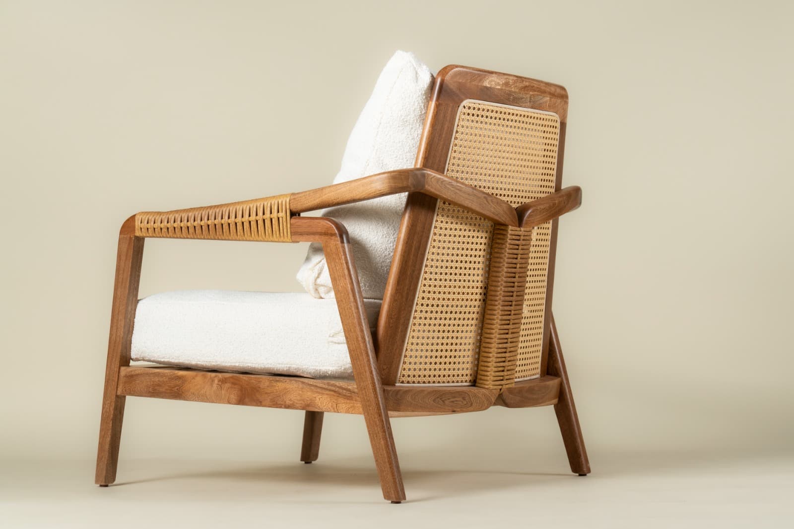 A wooden armchair with woven cane back and armrests. The chair has a plush white seat cushion and a matching lumbar pillow. The wooden frame exhibits a natural grain and is finished with a smooth sheen. The cane work is intricately woven, providing a textured contrast to the wood. — 3D model