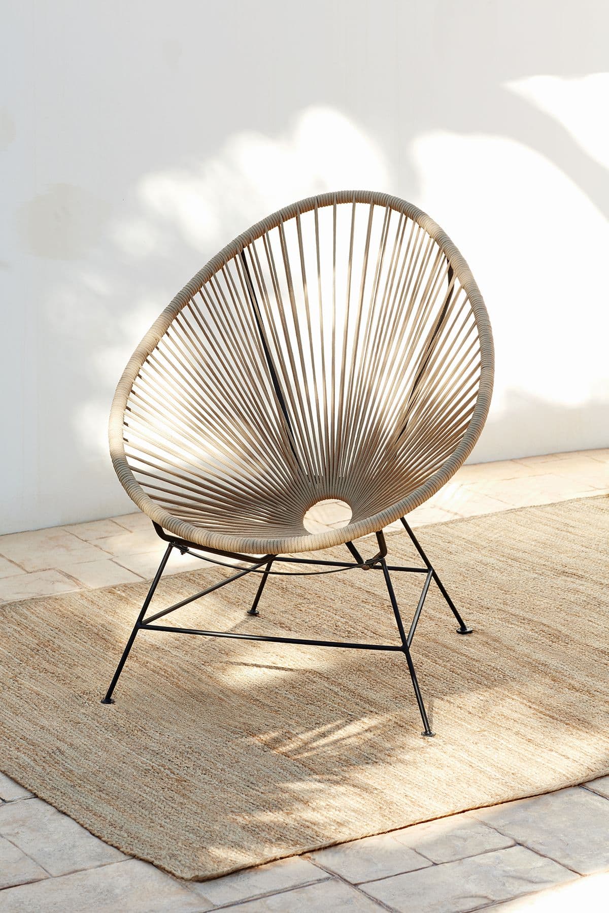 An Acapulco-style lounge chair featuring an egg-shaped seat crafted from radially woven beige or tan synthetic cord. The seat is supported by a minimalist, four-legged black metal frame, designed for comfort and outdoor durability. — 3D model