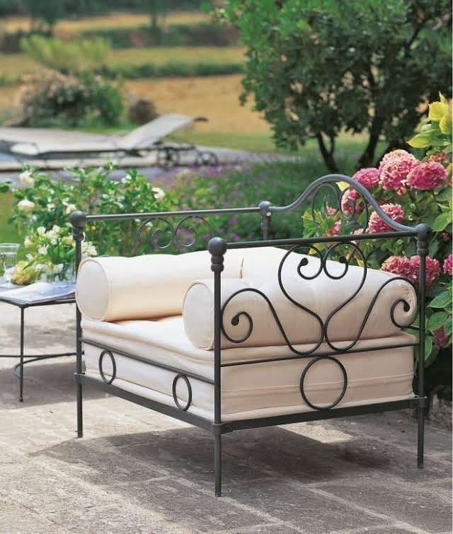 A small, ornate bed with a dark wrought iron frame and cream fabric cushions, featuring scrolled heart designs on the headboard/backrest and sides. — 3D model