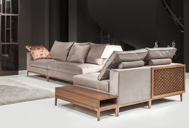 A modular sectional sofa with upholstered cushions and a decorative wooden side panel. The sofa has a low profile with slender wooden legs. It includes several plush throw pillows, one of which has an ornate patterned cover. A matching wooden coffee table with an open compartment is positioned in front of the sofa. — 3D model