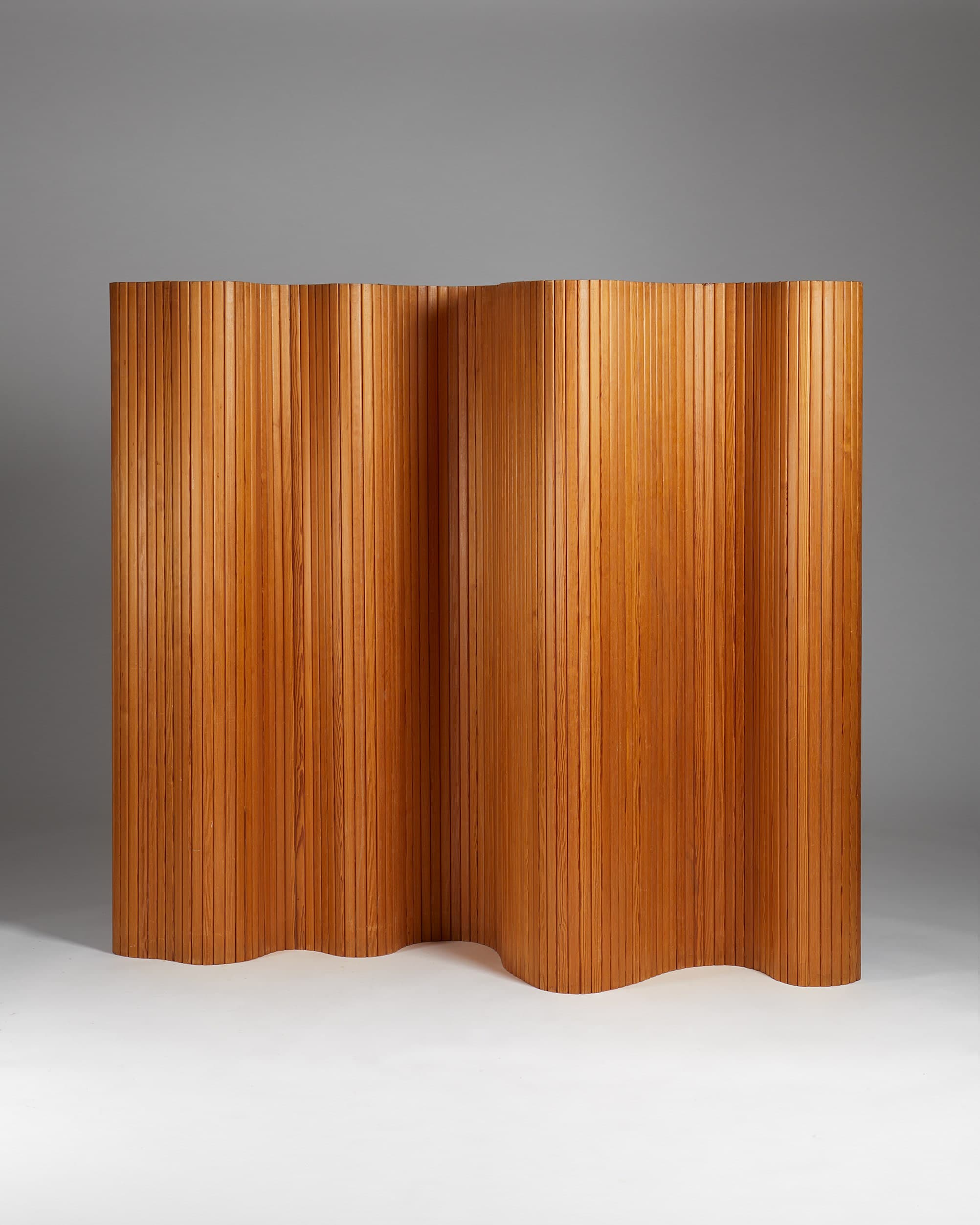 A room divider with a scalloped top and bottom edge, constructed from numerous thin, vertically oriented wooden slats. The slats are tightly spaced and appear to be made of bamboo or a similar pliable wood, giving the surface a textured, ribbed appearance. The divider exhibits a wave-like undulation across its width, creating depth and visual interest. — 3D model