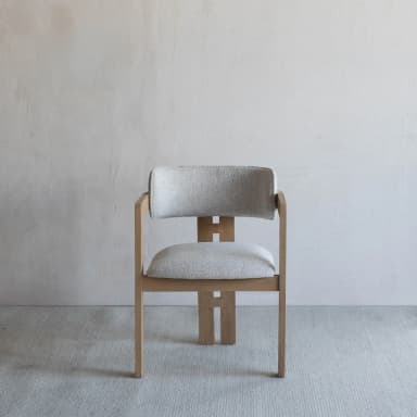 A contemporary dining chair featuring a light-toned wooden frame and light gray upholstered seat and backrest. The backrest is gently curved, providing integrated armrests as part of the overall wooden structure. The rear legs feature distinctive H-shaped vertical cutouts, adding to its modern aesthetic. — 3D model