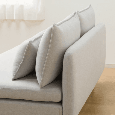 A contemporary armless chaise loveseat, upholstered in a light gray textured fabric. It features a low-profile design with a deep, elongated seat on the right side, resembling a chaise. The seating is supported by minimalist black metal legs, and the piece includes two large back cushions and two smaller rectangular throw pillows, all with subtle piped edges. — 3D model