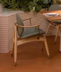 A contemporary armchair featuring a light-toned wooden frame with a gently curved backrest and integrated armrests. The seat and backrest are upholstered in a light blue-green fabric, providing a soft contrast to the wood. Brass accents are visible on the armrest joints and leg tips, adding a touch of sophistication. The legs are tapered, contributing to the chair's refined and modern aesthetic. — 3D model