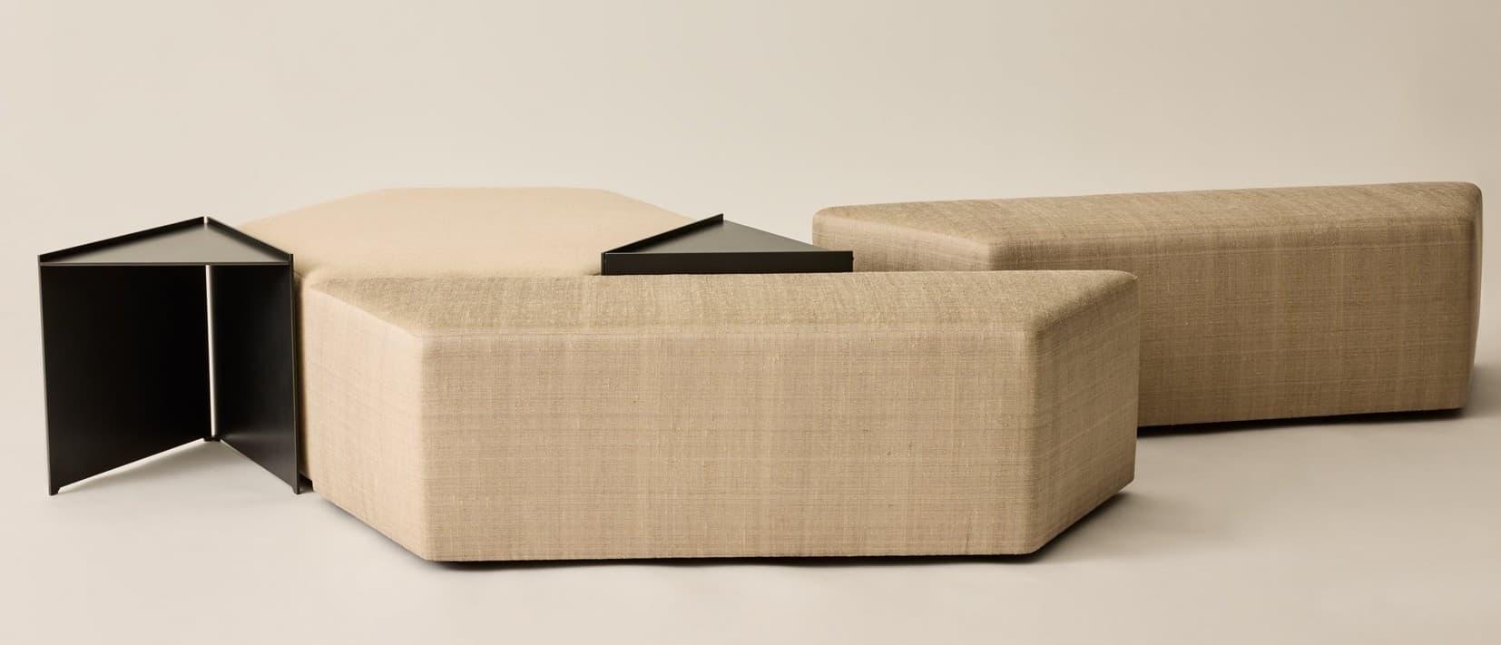 A modular seating arrangement composed of multiple upholstered ottomans of varying geometric shapes. The pieces are covered in a textured, woven fabric. Integrated into the design are sharp-edged, triangular black metal elements, one appearing as a small table surface and another as an architectural-like structure with a triangular peak. The forms are curvilinear and angular, suggesting a contemporary or abstract design. — 3D model