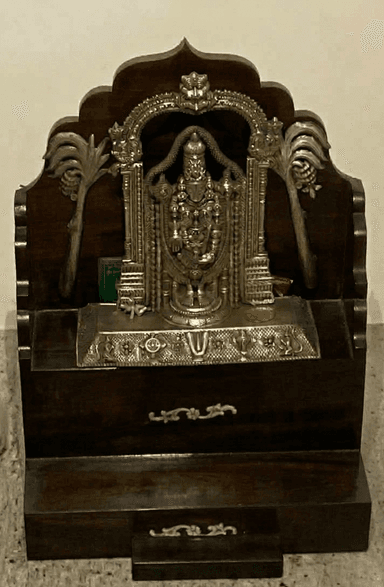 A traditional Indian pooja mandir, a small home temple crafted from dark-stained wood, featuring a decorative silver-plated archway and a deity idol. The structure includes a main platform for the idol and small pull-out drawers for storage of ritual items. — 3D model
