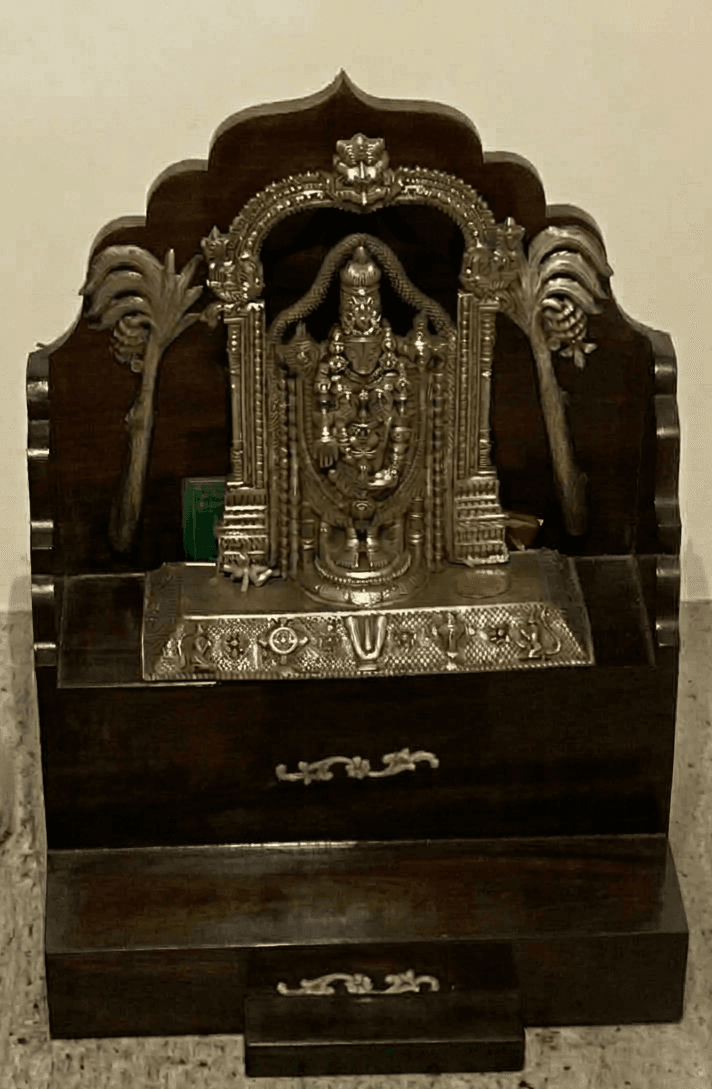 A traditional Indian pooja mandir, a small home temple crafted from dark-stained wood, featuring a decorative silver-plated archway and a deity idol. The structure includes a main platform for the idol and small pull-out drawers for storage of ritual items. — 3D model