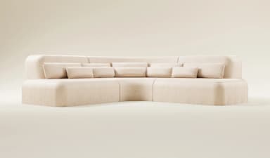 A modular, sectional sofa with a curved design and plush upholstery. It features a low profile with rounded corners and is complemented by multiple scatter cushions. The sofa appears to be constructed from a fabric material and is arranged in an L-shape. — 3D model
