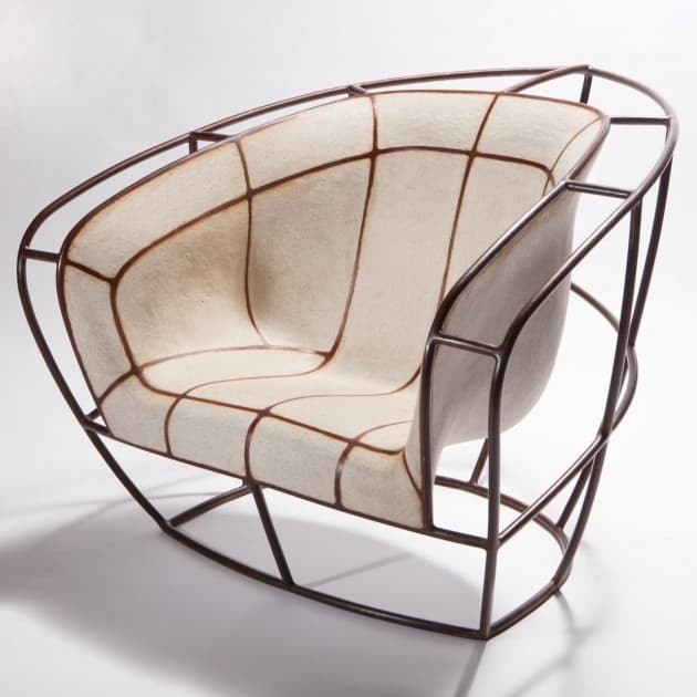 A modern armchair with a distinct curvilinear design. The chair features an external frame constructed from dark, possibly metal, tubing that forms a geometric cage-like structure. Inside this frame, a molded seat and backrest are visible, appearing to be made of a textured, cream-colored material segmented by dark brown lines forming a grid-like pattern. The overall form suggests an artistic and sculptural approach to furniture design. — 3D model