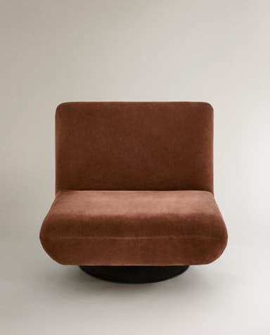 A contemporary armchair with a low profile and plush upholstery. The chair features a rounded silhouette, a supportive backrest, and a deep seat. It is mounted on a circular, black swivel base, allowing for 360-degree rotation. The fabric appears to have a soft, velvety texture. — 3D model