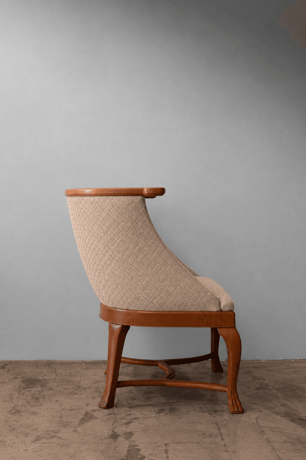 A refined barrel-back armchair featuring a solid wood frame with a polished light brown finish. The chair's back and seat are upholstered in a textured beige fabric with a distinctive diamond quilting pattern. The continuous back curves gracefully to form integrated, low-profile armrests. The chair is supported by four tapered, carved wooden legs, connected by an elegant stretcher base. — 3D model