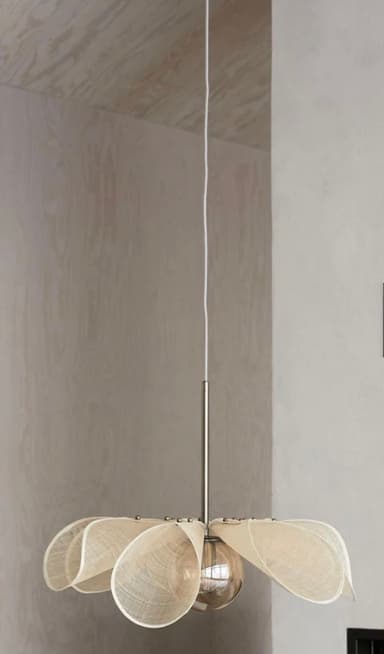 A contemporary pendant light featuring a shade composed of multiple off-white, petal-shaped fabric elements. These elements are arranged radially around a central brass stem, connected by small brass studs, creating an organic, floral silhouette. A single exposed light bulb is positioned at the center, underneath the fabric petals. The fixture hangs from a single white electrical cord connected to the brass stem. — 3D model