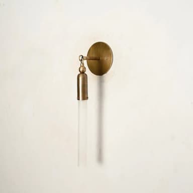 A modern wall sconce featuring a circular brass wall plate, an articulating arm, and a cylindrical brass housing holding a frosted glass rod-shaped shade. — 3D model