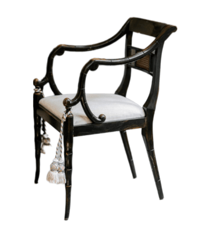 An armchair featuring an ebonized, faux bamboo-style wooden frame. The backrest includes a rectangular woven cane panel, while the arms are elegantly curved, flowing from the back. The seat is upholstered in a light-colored, possibly off-white or cream, fabric. The legs are tapered and also mimic the bamboo motif, with the front legs adorned with decorative tassels. The overall aesthetic suggests a Regency or Chinoiserie influence. — 3D model