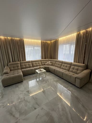 A contemporary modular U-shaped sectional sofa upholstered in a neutral beige woven fabric, featuring button-tufted seat and back cushions and integrated low-profile armrests. The configuration includes a chaise lounge on one end. — 3D model