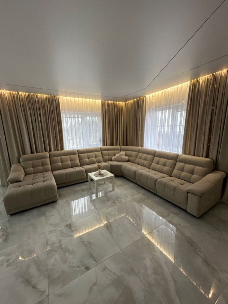 A contemporary modular U-shaped sectional sofa upholstered in a neutral beige woven fabric, featuring button-tufted seat and back cushions and integrated low-profile armrests. The configuration includes a chaise lounge on one end. — 3D model