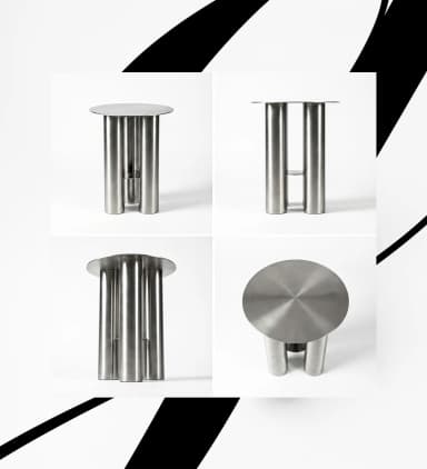 A small, round accent table constructed entirely from brushed stainless steel. It features a circular top supported by three large, cylindrical legs. One of the legs appears to be composed of two half-cylinders or has a vertical cutout, revealing a smaller internal cylindrical element or a void, adding a distinctive design element. The overall aesthetic is minimalist, modern, and industrial. — 3D model