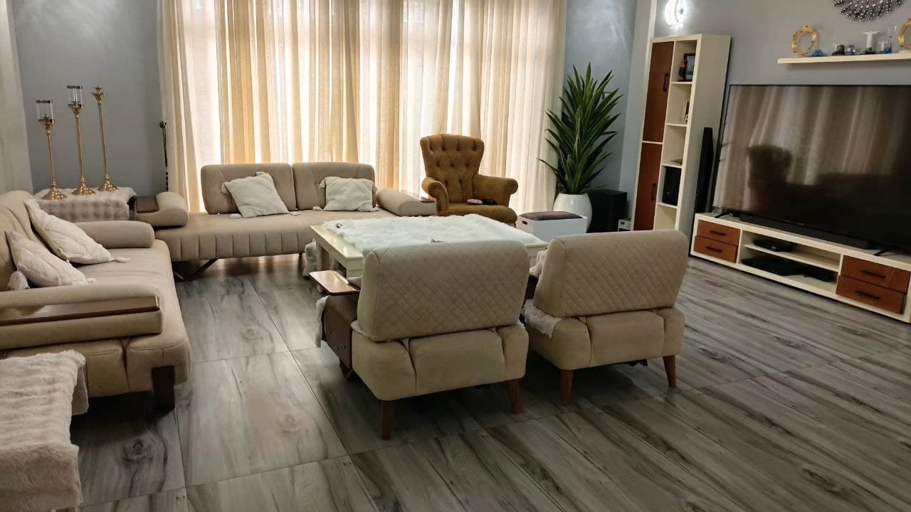 A three-seater contemporary sofa featuring light beige fabric upholstery, distinct quilted backrests, and integrated wooden elements on the armrests and as an exposed frame detail along the base. — 3D model