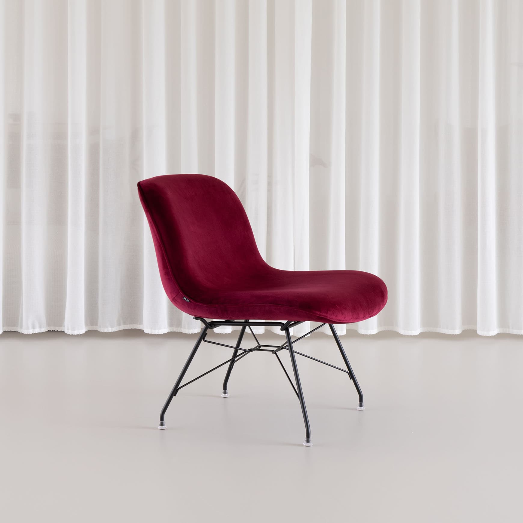 A modern armless chair upholstered in deep red velvet, featuring a shell-shaped seat and back, supported by slender black metal legs. — 3D model