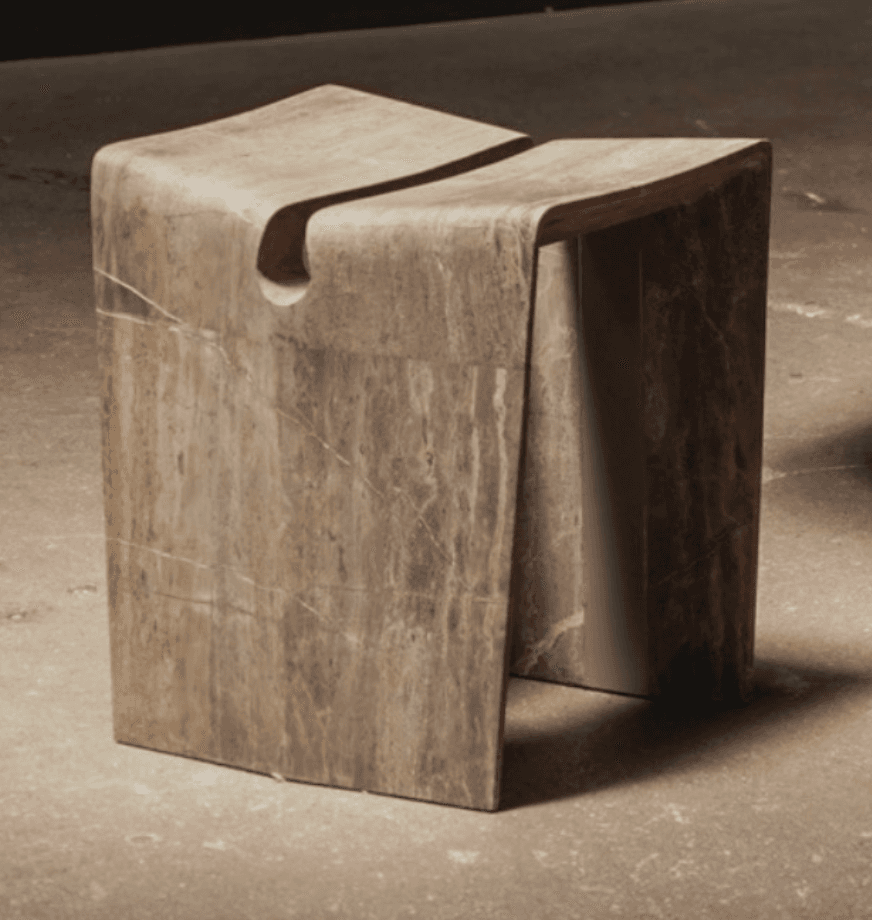 A small, contemporary sculptural stool crafted from natural marble, featuring a monolithic, curved form with a distinctive split-top design and visible veining. — 3D model