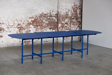 A long, modular dining table featuring three distinct segments with rounded ends, supported by a vibrant blue tubular metal frame. Each segment's top is dark blue, complementing the bright blue base, with small green connectors and feet accents. — 3D model