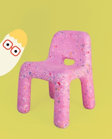 A small, child-sized chair made entirely from a single molded piece of recycled plastic, featuring a distinctive speckled or confetti-like pattern. The chair is predominantly white with multi-colored fragments (red, orange, yellow, blue, green) embedded throughout the material. It has a simple, monolithic design with rounded edges and a backrest, and an oval cutout in the seat. — 3D model