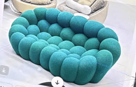 A contemporary loveseat composed of numerous individually upholstered spherical or ovoid modules, arranged to form a continuous seating surface and integrated backrest. The upholstery features a gradient color scheme, transitioning from a darker blue-green to a lighter teal-green hue across its length. — 3D model