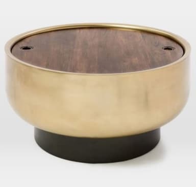 A round coffee table with a wood-grain effect tabletop and a brushed brass-finished cylindrical body, supported by a dark, circular base. The tabletop has two small, recessed black circular elements, possibly for lid attachment or decorative purposes. — 3D model
