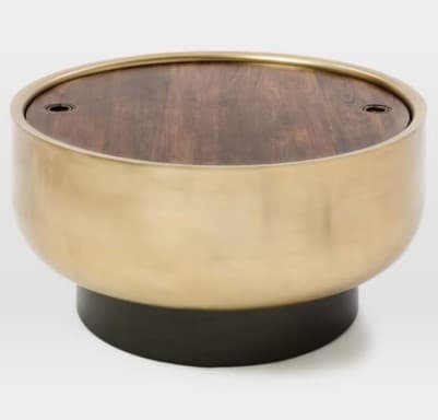A round coffee table with a wood-grain effect tabletop and a brushed brass-finished cylindrical body, supported by a dark, circular base. The tabletop has two small, recessed black circular elements, possibly for lid attachment or decorative purposes. — 3D model
