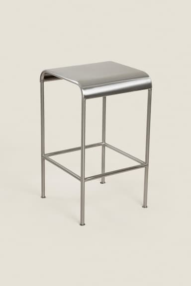 A minimalist, square-top stool constructed entirely from brushed stainless steel. It features a solid, slightly curved seat, supported by four slender tubular legs. The legs are connected by a lower square frame that serves as a footrest, enhancing stability and user comfort. The design is clean and contemporary, with visible welds suggesting a robust construction. The overall finish is a matte silver, indicating a brushed or satin metal surface. — 3D model