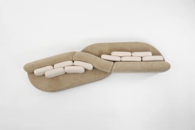 A contemporary curved modular sectional sofa featuring a beige upholstered base and lighter, off-white rectangular back cushions. The sofa consists of at least two large, organically shaped sections joined to form a fluid, undulating seating arrangement. — 3D model