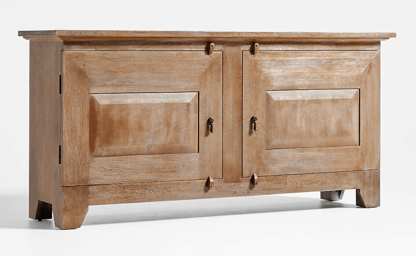A rustic distressed wood sideboard cabinet with a light, weathered finish. It features a rectangular top, two cabinet doors with raised panel details, and simple dark metal ring pull handles and visible hinges. The cabinet stands on short, recessed block feet. — 3D model