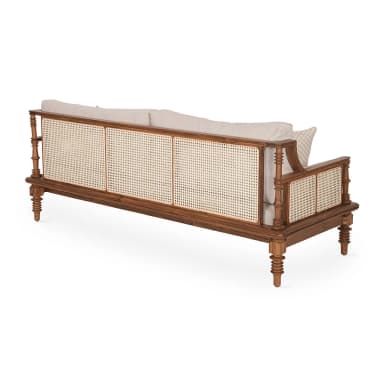 A three-seater sofa featuring a robust exposed wooden frame with a natural finish, intricate woven cane panels on the armrests, and turned legs. It is upholstered with thick, light beige fabric seat and back cushions, accompanied by two matching bolster pillows and two patterned throw pillows. — 3D model