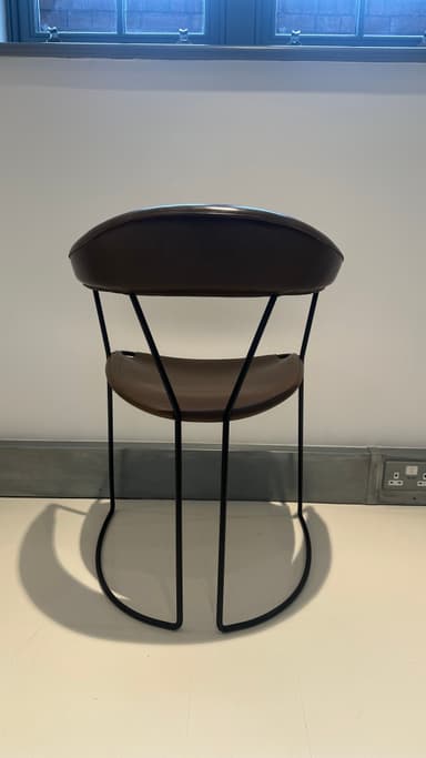 A contemporary armchair with a dark brown leather seat and backrest supported by a slender black metal frame. The frame features a curved base that extends into the legs, providing stability and a dynamic visual element. The seat and backrest are subtly contoured for comfort and appear to be constructed from stitched leather panels. — 3D model