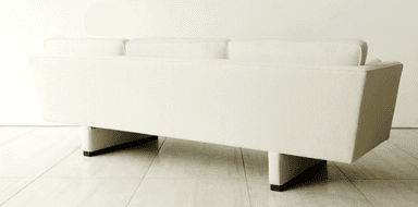 A contemporary three-seater sofa upholstered in an off-white bouclé-like fabric, featuring a single button-tufted seat cushion, three loose back cushions, and integrated wide arms resting on a recessed, block-like base. — 3D model