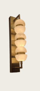 A contemporary wall-mounted light fixture, characterized by a rectangular brass backplate and a vertical column of six spherical alabaster diffusers. Each diffuser is composed of two half-spheres separated by a narrow gap, held in place by slim brass rings, creating a layered, luminous effect. The light emanates a soft, warm glow through the translucent alabaster. — 3D model