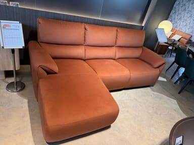 An L-shaped sectional sofa upholstered in a warm terracotta-colored fabric, featuring an integrated chaise lounge, plump back cushions, and gently rolled armrests. — 3D model